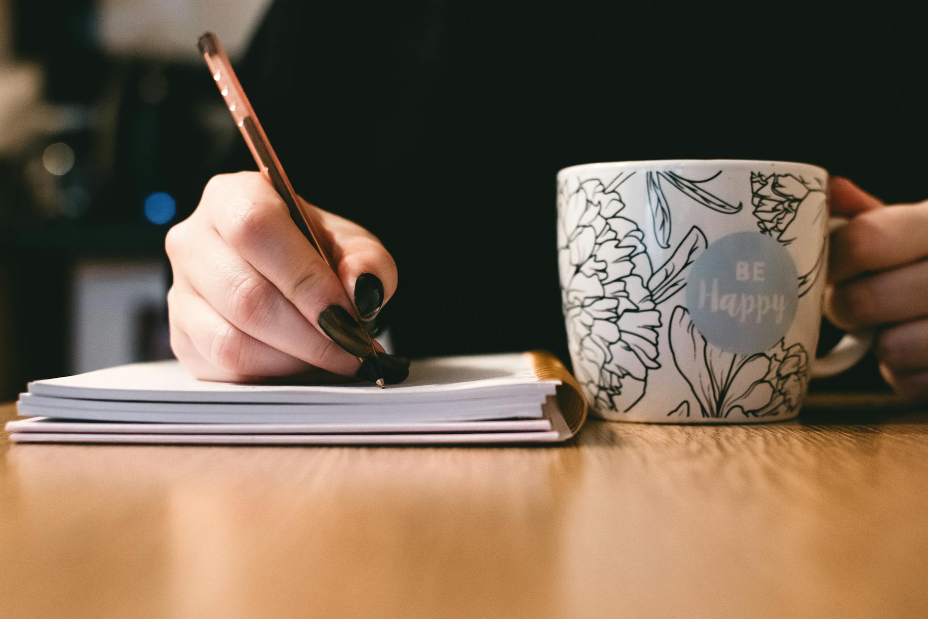 woman writing with a coffee/tea mug that says "be happy"